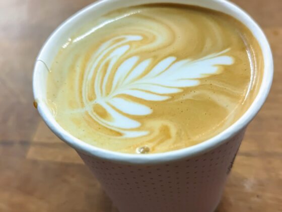 kelímek s cappuccinem a latte artem na dřevěném stole