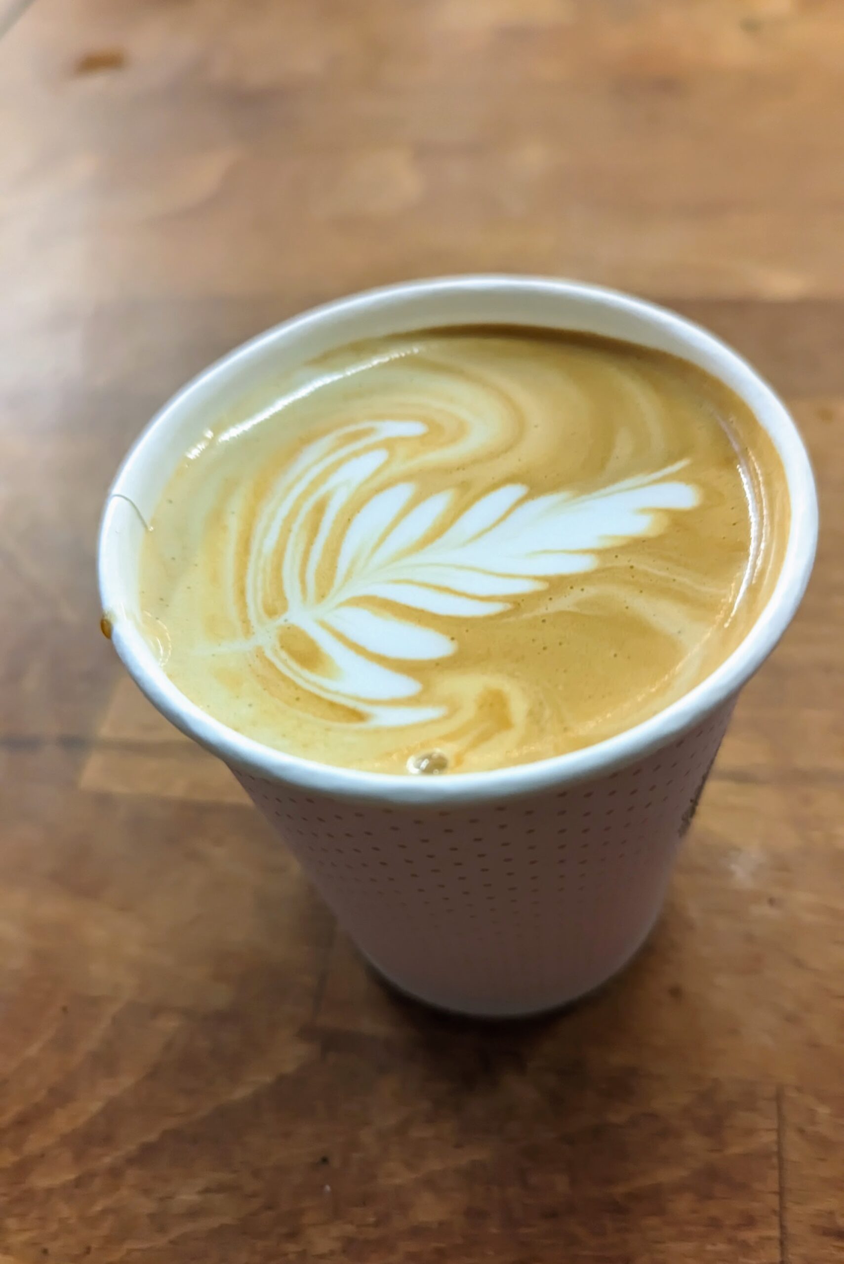 kelímek s cappuccinem a latte artem na dřevěném stole
